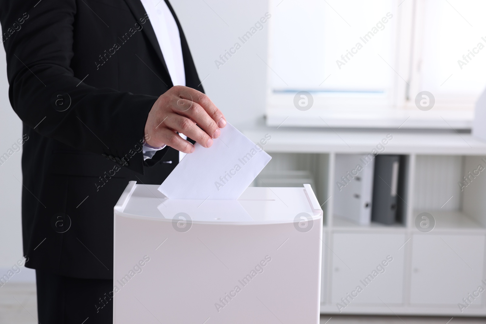 Photo of Man putting his vote into ballot box indoors, closeup. Space for text