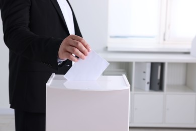 Man putting his vote into ballot box indoors, closeup. Space for text