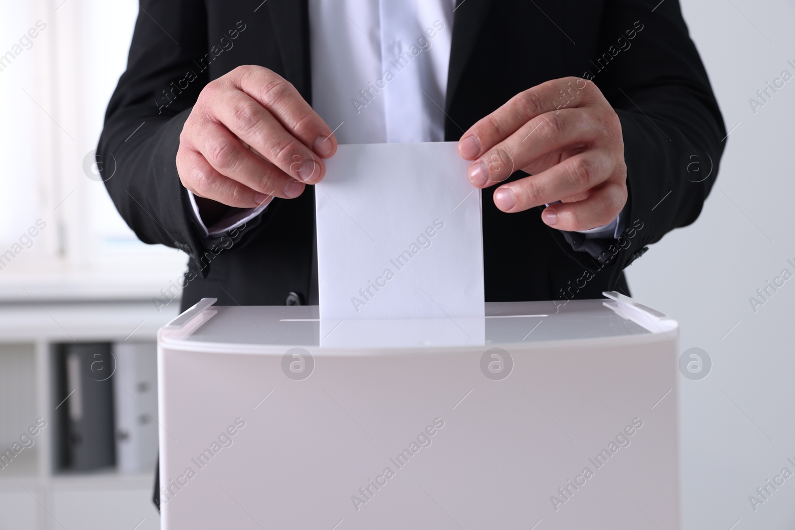 Photo of Man putting his vote into ballot box indoors, closeup