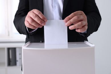 Photo of Man putting his vote into ballot box indoors, closeup