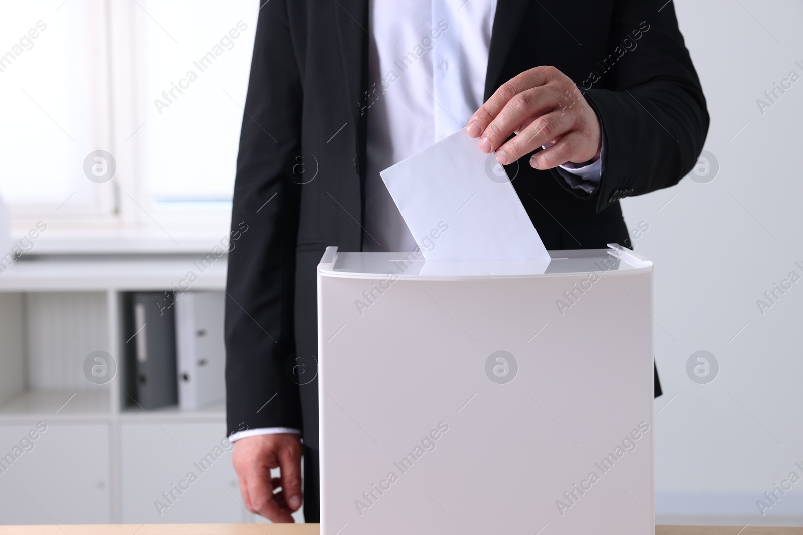 Photo of Man putting his vote into ballot box indoors, closeup