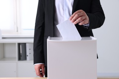 Photo of Man putting his vote into ballot box indoors, closeup