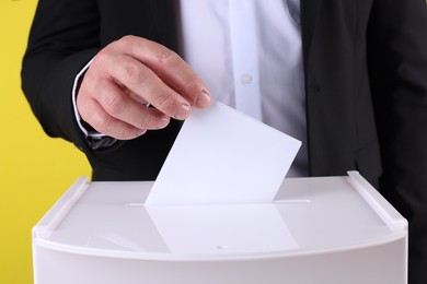 Photo of Man putting his vote into ballot box against yellow background, closeup