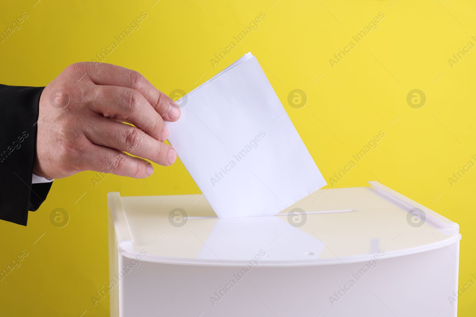 Photo of Man putting his vote into ballot box against yellow background, closeup