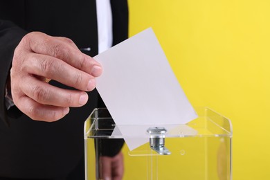 Photo of Man putting his vote into ballot box against yellow background, closeup