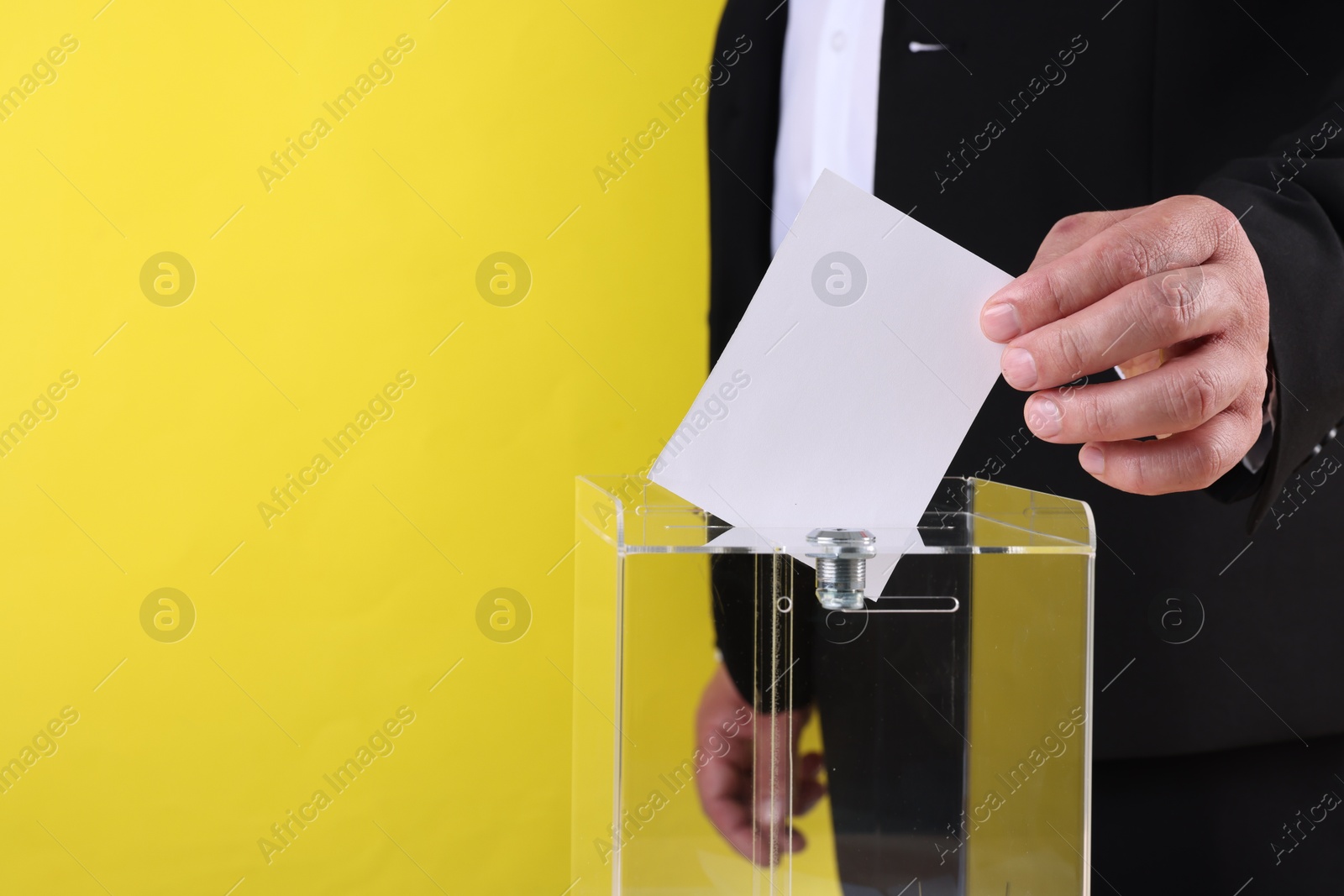 Photo of Man putting his vote into ballot box against yellow background, closeup. Space for text