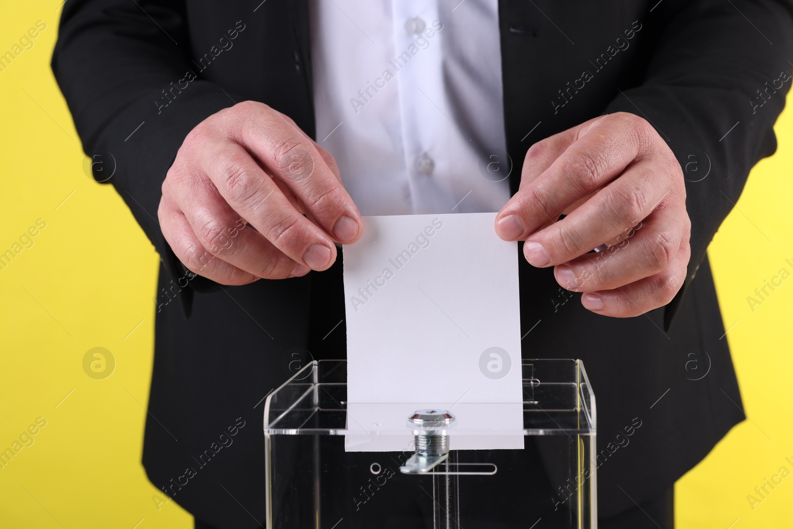 Photo of Man putting his vote into ballot box against yellow background, closeup