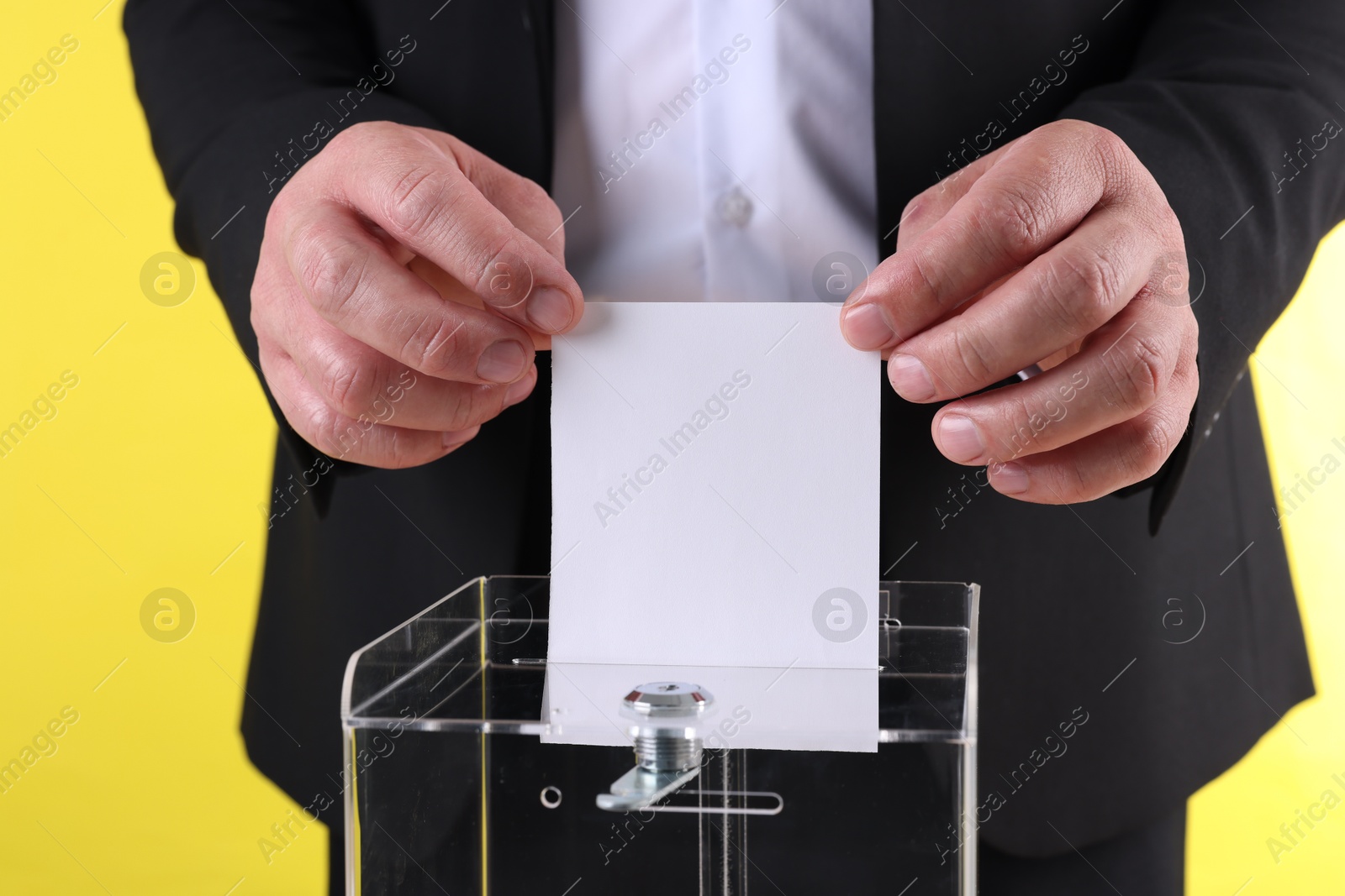 Photo of Man putting his vote into ballot box against yellow background, closeup