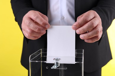 Photo of Man putting his vote into ballot box against yellow background, closeup