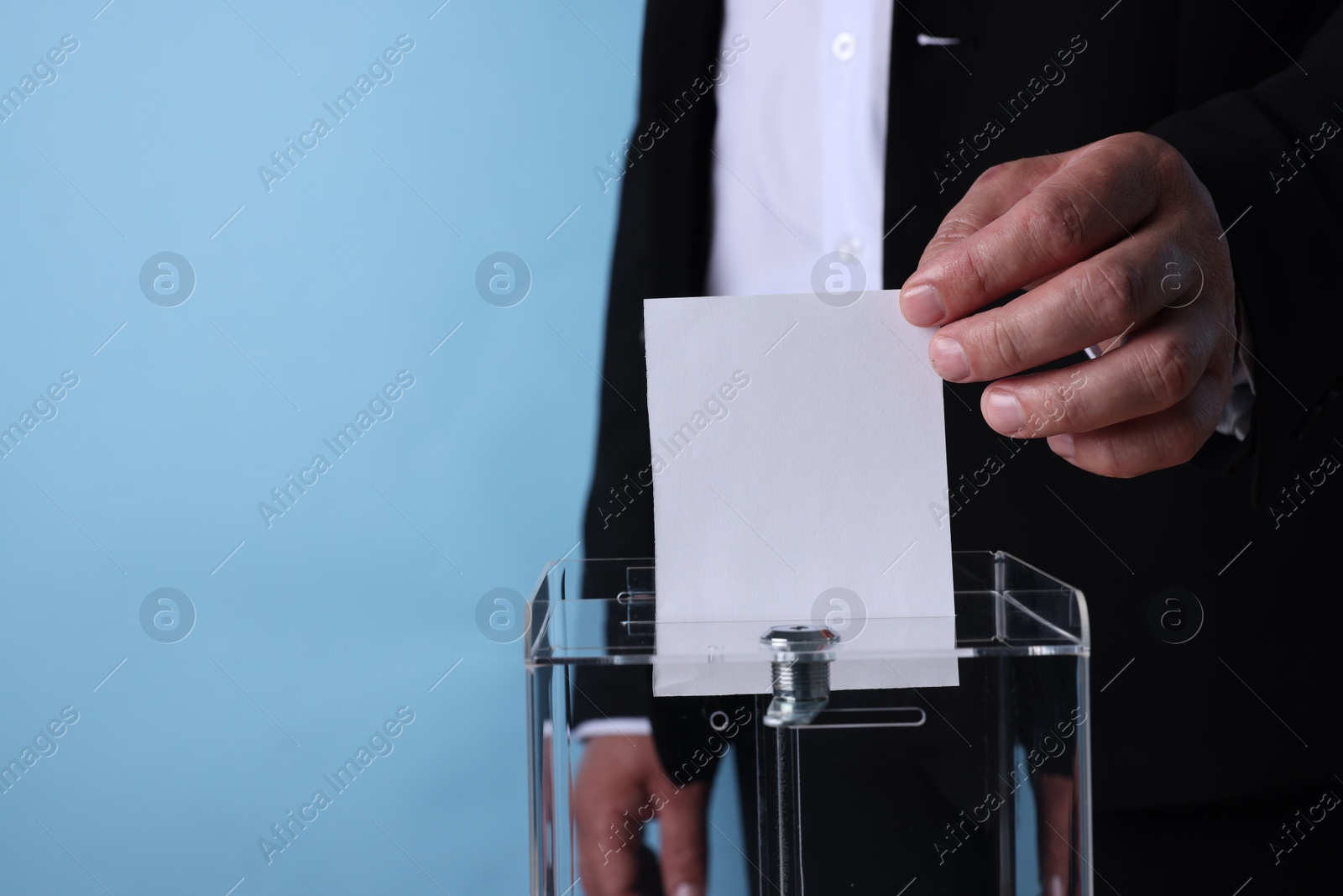 Photo of Man putting his vote into ballot box against light blue background, closeup. Space for text