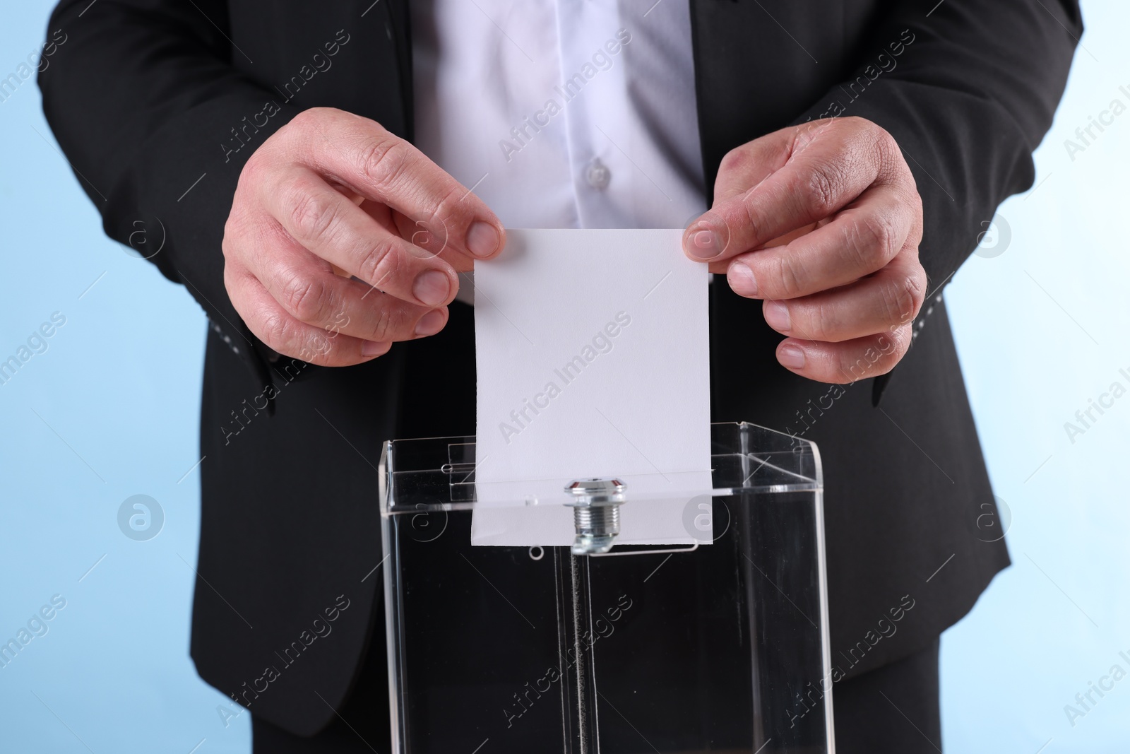 Photo of Man putting his vote into ballot box against light blue background, closeup