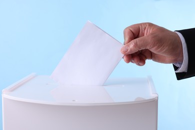 Photo of Man putting his vote into ballot box against light blue background, closeup