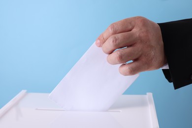 Photo of Man putting his vote into ballot box against light blue background, closeup