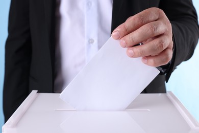 Photo of Man putting his vote into ballot box against light blue background, closeup