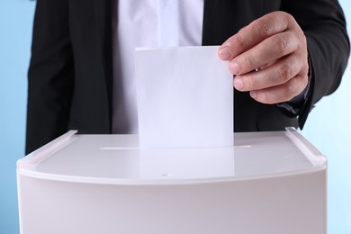 Photo of Man putting his vote into ballot box against light blue background, closeup