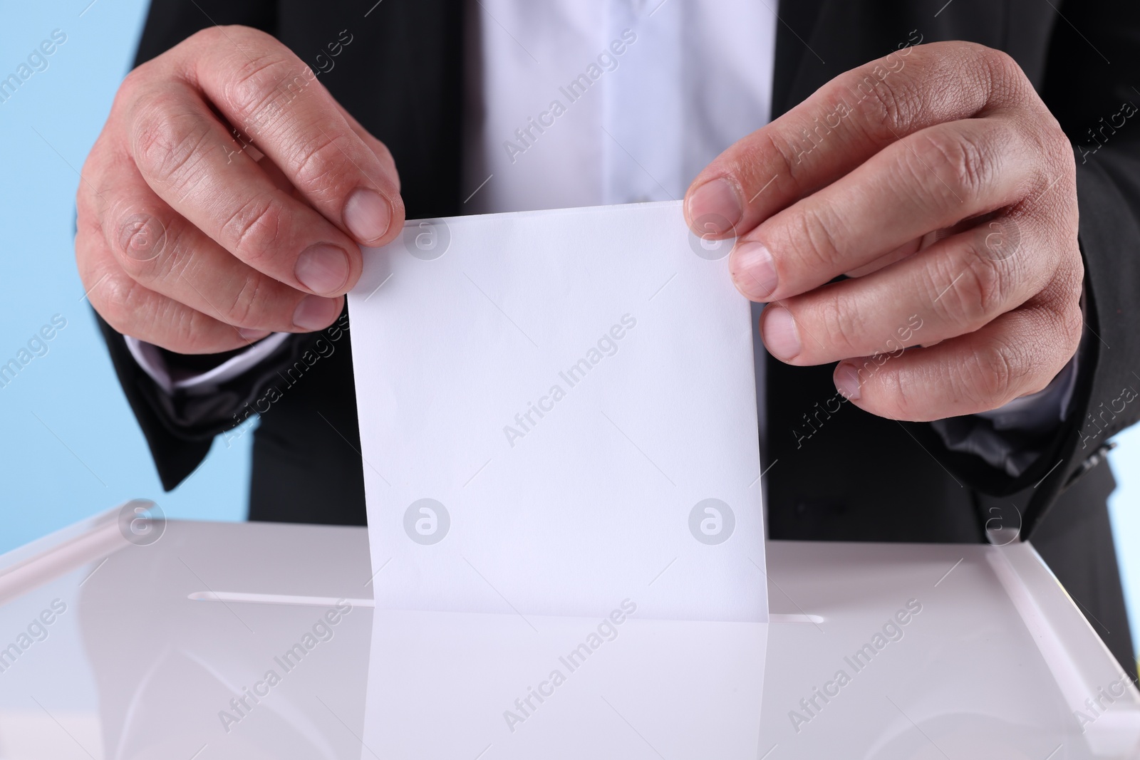 Photo of Man putting his vote into ballot box against light blue background, closeup