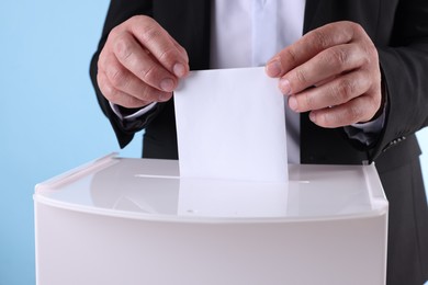 Photo of Man putting his vote into ballot box against light blue background, closeup