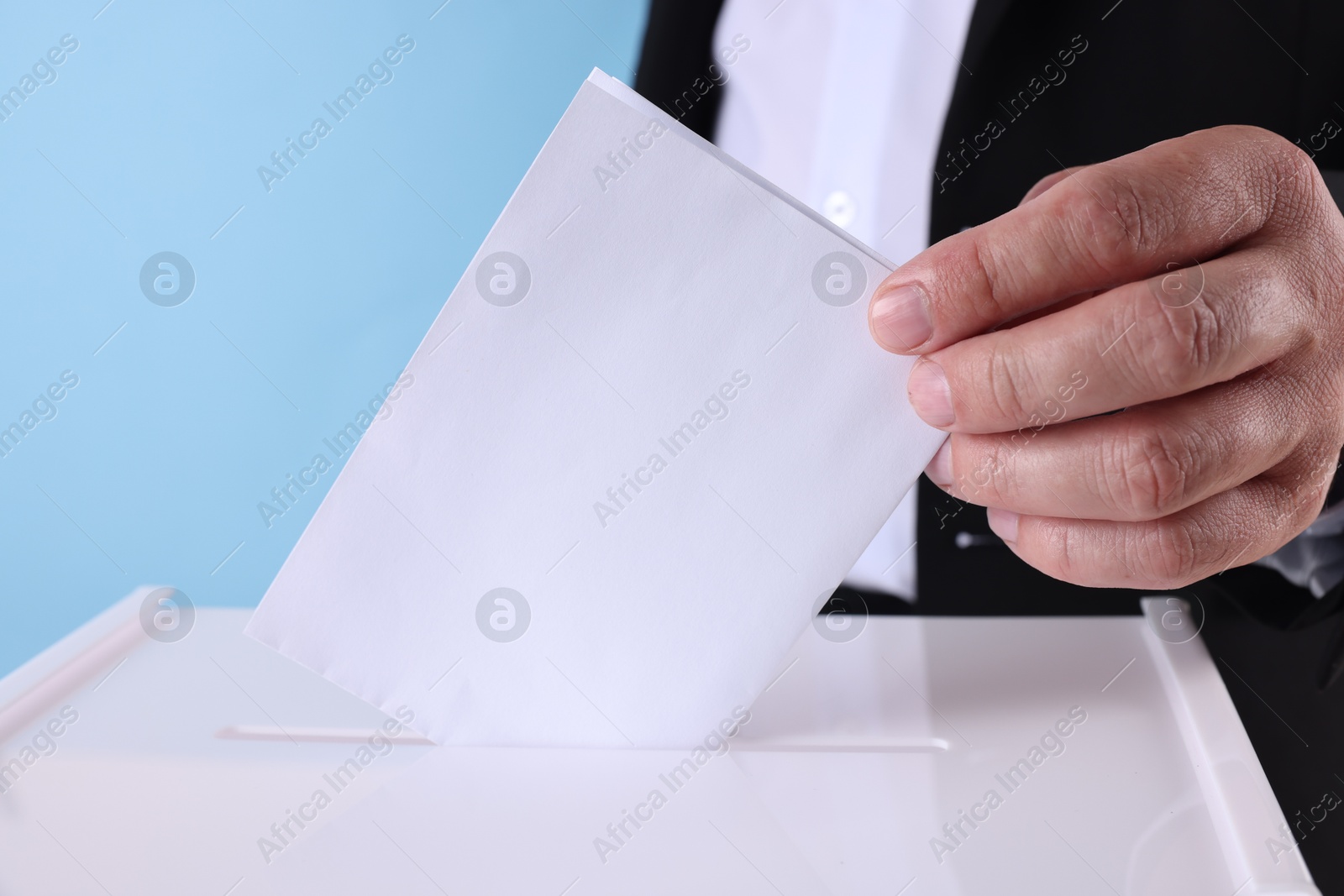 Photo of Man putting his vote into ballot box against light blue background, closeup