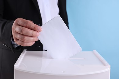 Photo of Man putting his vote into ballot box against light blue background, closeup