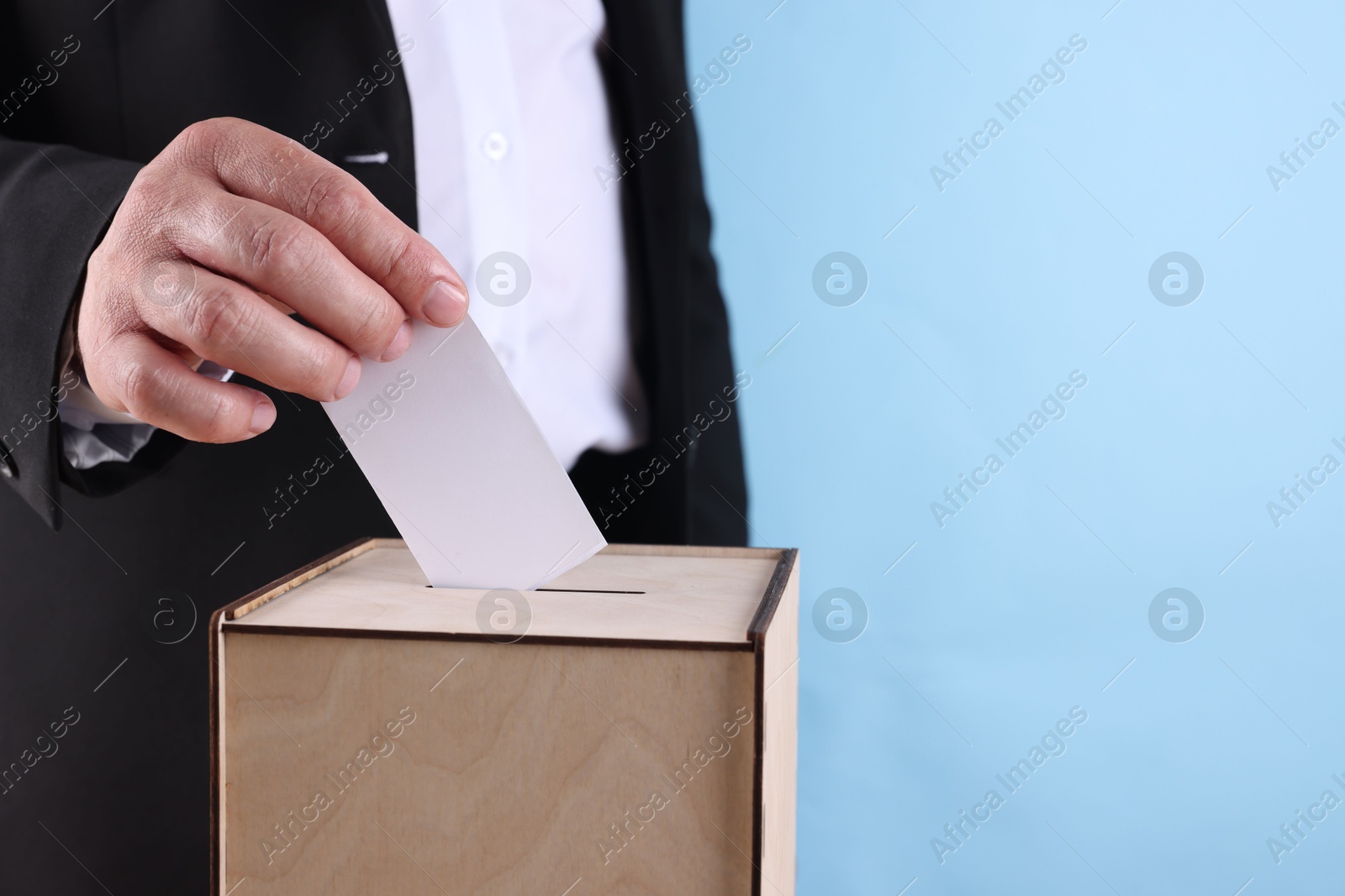 Photo of Man putting his vote into ballot box against light blue background, closeup. Space for text