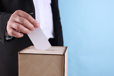 Photo of Man putting his vote into ballot box against light blue background, closeup. Space for text