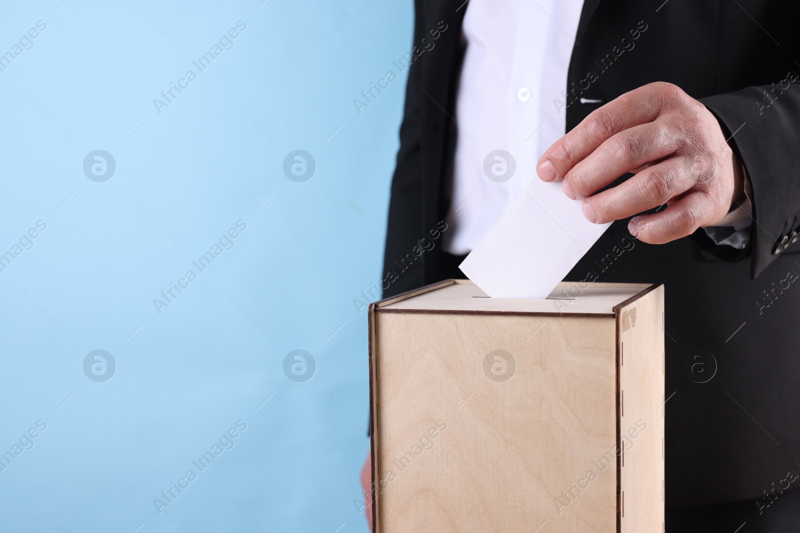 Photo of Man putting his vote into ballot box against light blue background, closeup. Space for text