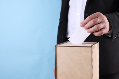 Photo of Man putting his vote into ballot box against light blue background, closeup. Space for text