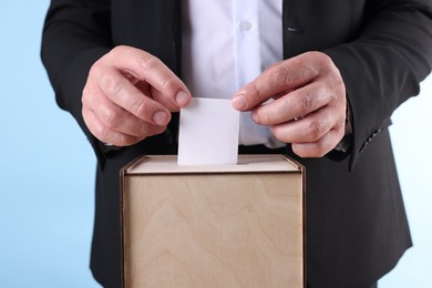 Photo of Man putting his vote into ballot box against light blue background, closeup