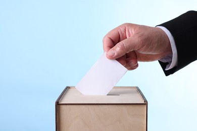 Photo of Man putting his vote into ballot box against light blue background, closeup