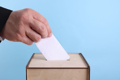 Photo of Man putting his vote into ballot box against light blue background, closeup