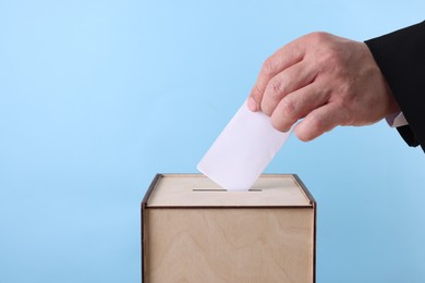 Photo of Man putting his vote into ballot box against light blue background, closeup