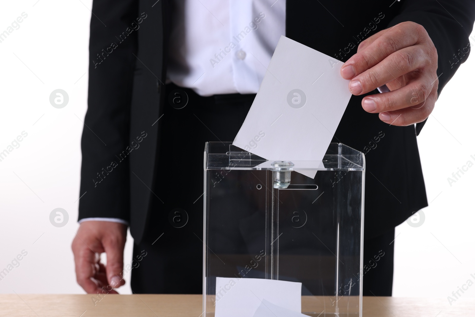 Photo of Man putting his vote into ballot box at table against white background, closeup