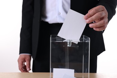 Photo of Man putting his vote into ballot box at table against white background, closeup