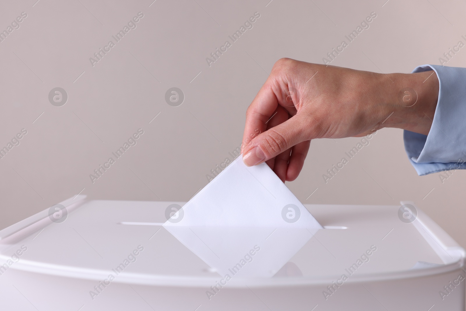 Photo of Woman putting her vote into ballot box against grey background, closeup