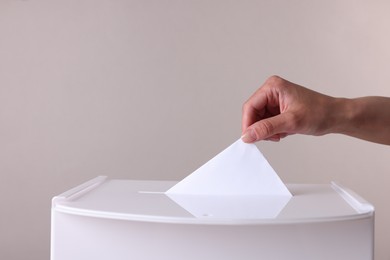 Photo of Woman putting her vote into ballot box against grey background, closeup