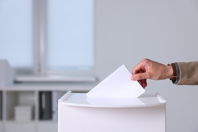 Photo of Woman putting her vote into ballot box indoors, closeup