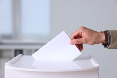 Photo of Woman putting her vote into ballot box indoors, closeup