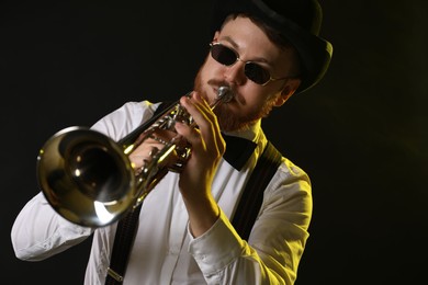 Photo of Professional musician playing trumpet on black background in color lights