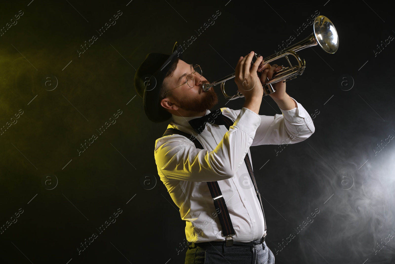 Photo of Professional musician playing trumpet on black background in color lights and smoke