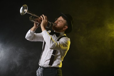 Photo of Professional musician playing trumpet on black background in color lights and smoke