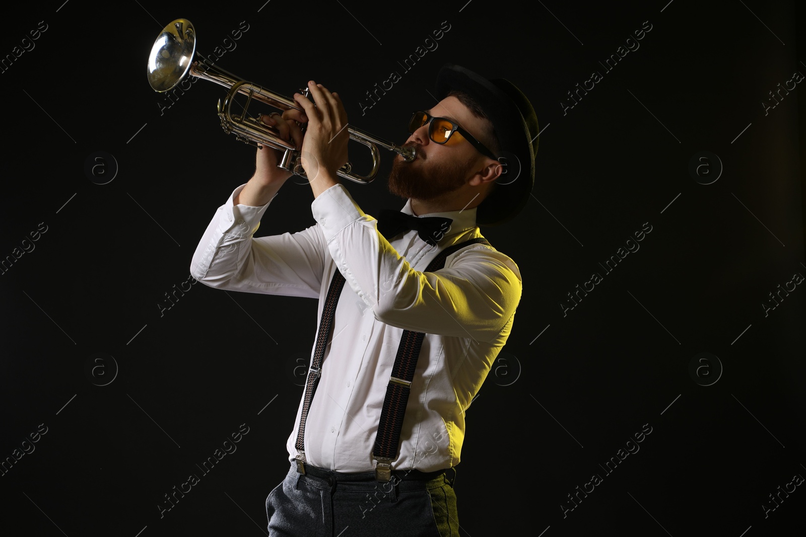 Photo of Professional musician playing trumpet on black background in color lights