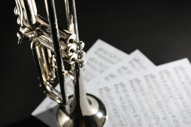 Photo of Closeup view of shiny trumpet and music sheets on dark background, space for text. Wind musical instrument