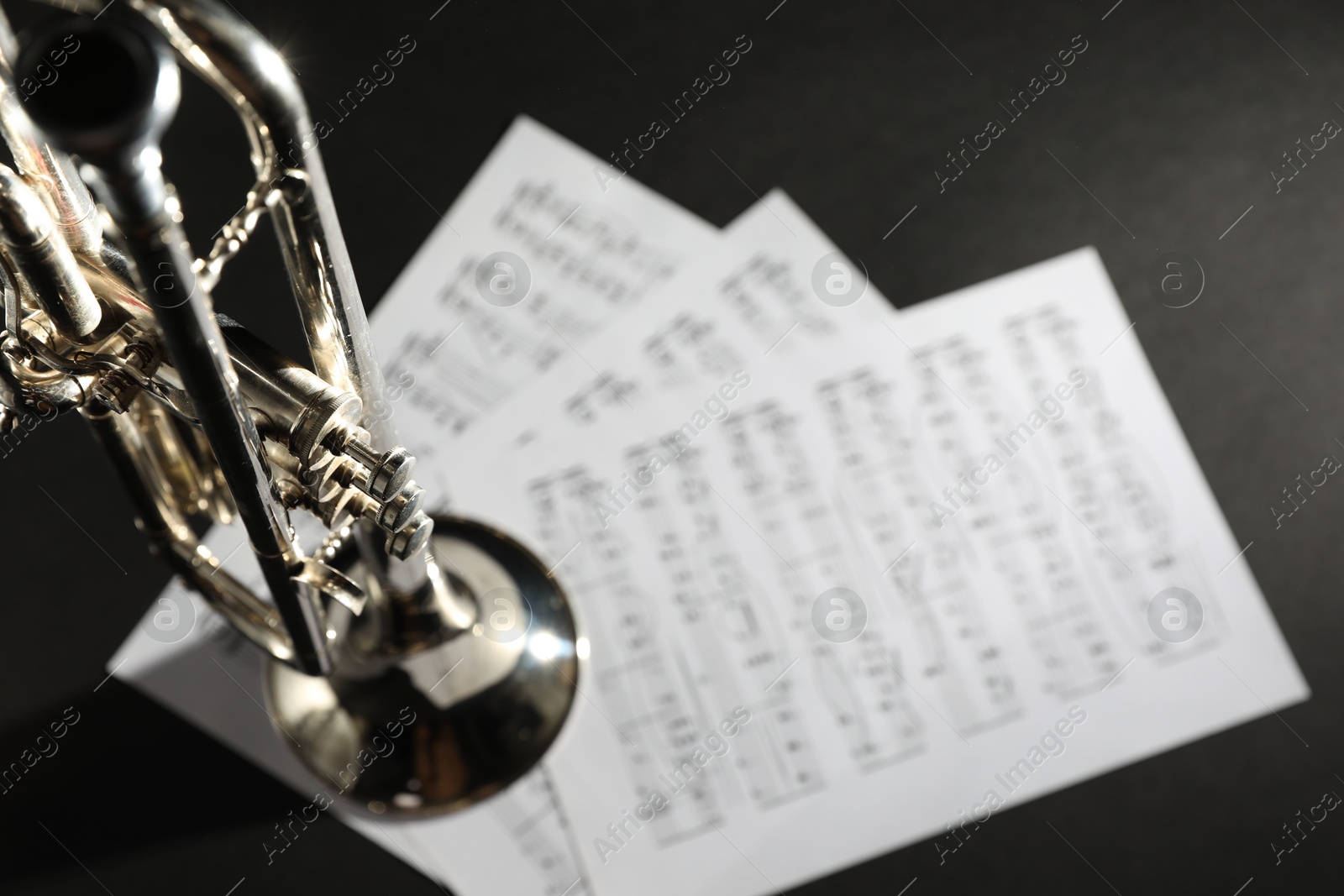 Photo of Closeup view of shiny trumpet and music sheets on dark background, space for text. Wind musical instrument