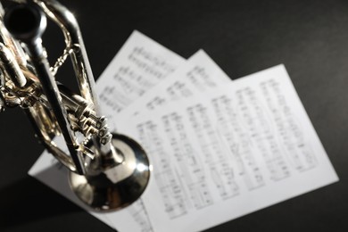 Closeup view of shiny trumpet and music sheets on dark background, space for text. Wind musical instrument