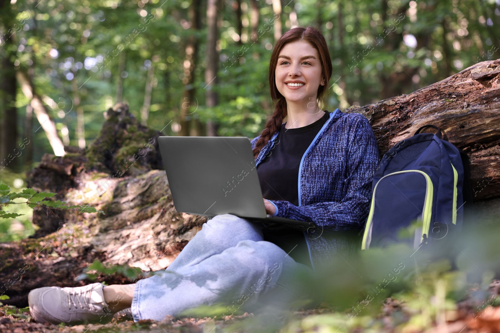 Photo of Smiling freelancer working with laptop in forest, low angle view. Remote job