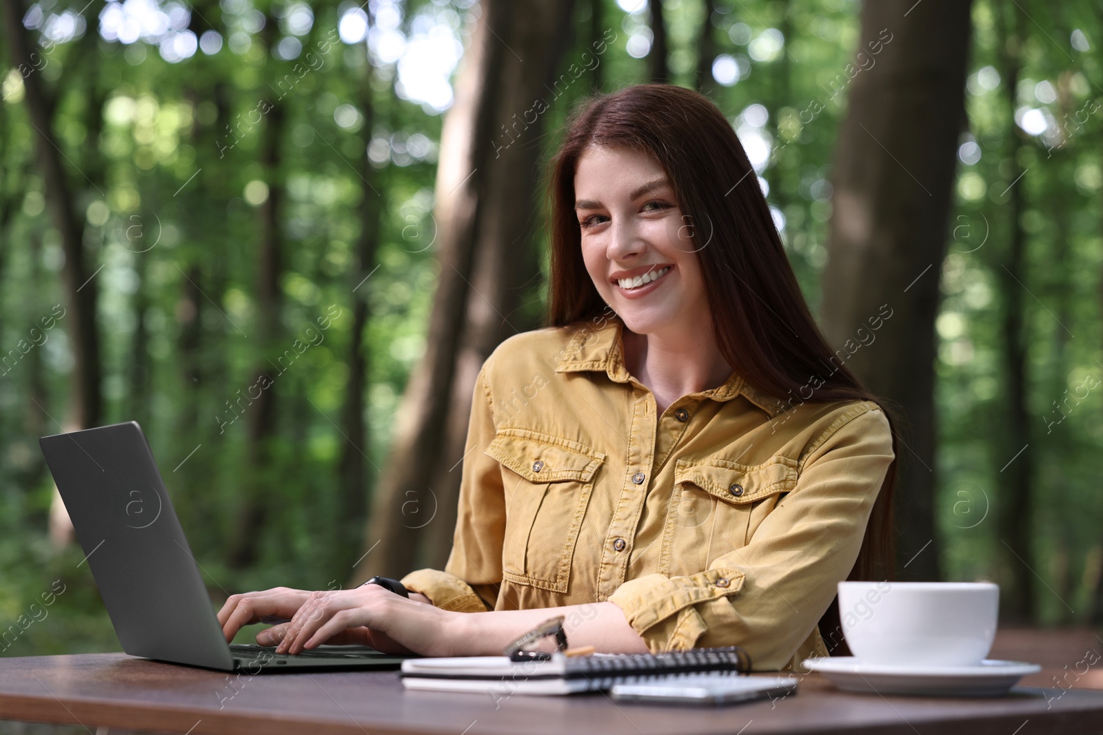 Photo of Smiling freelancer working with laptop at table outdoors. Remote job