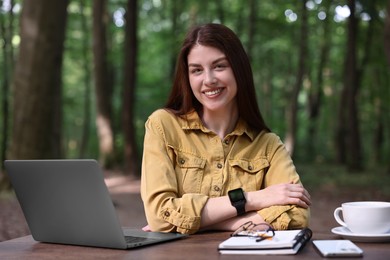 Photo of Smiling freelancer working with laptop at table outdoors. Remote job