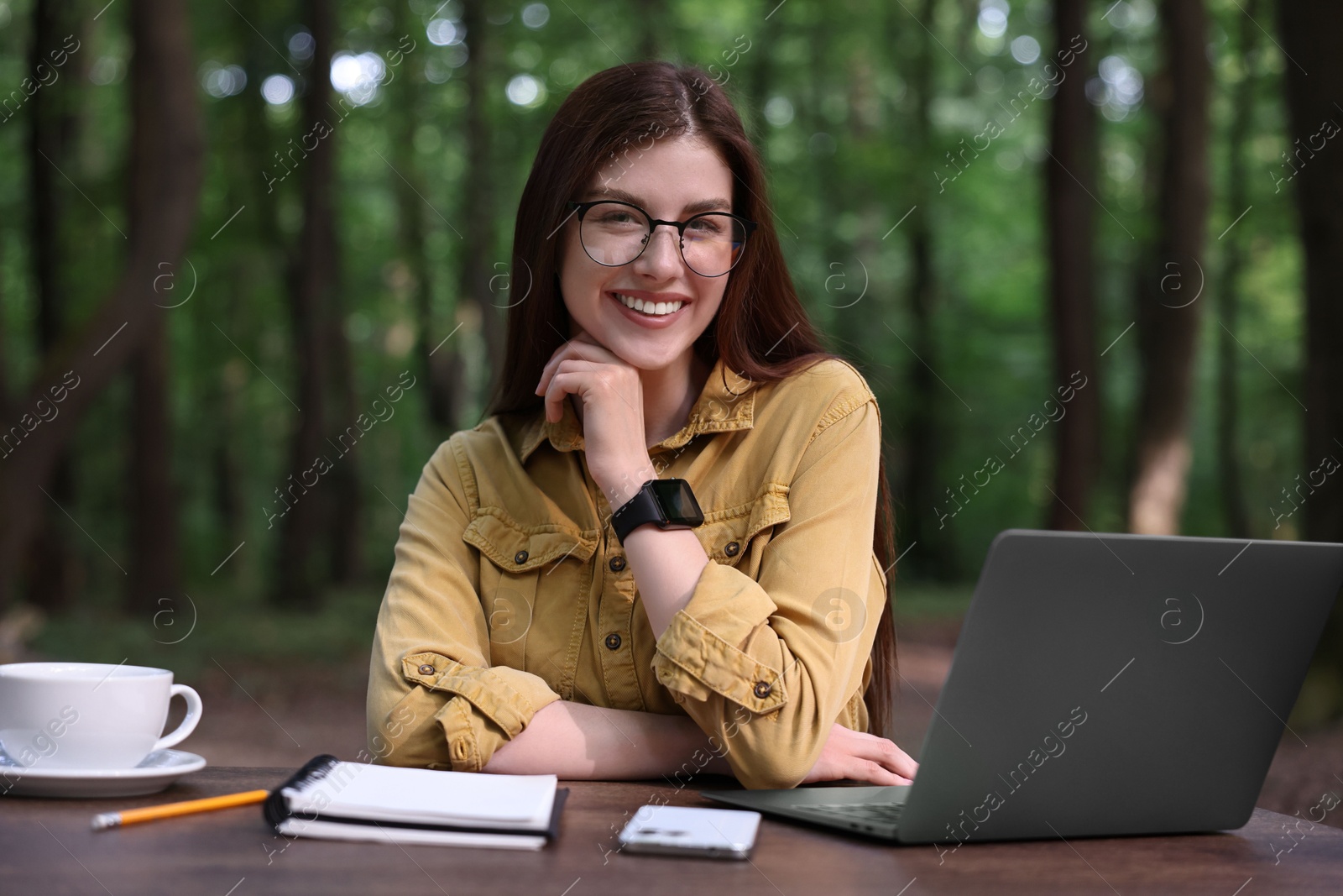 Photo of Smiling freelancer working with laptop at table outdoors. Remote job