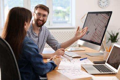 Cartographers working with cadastral map on computer at table in office