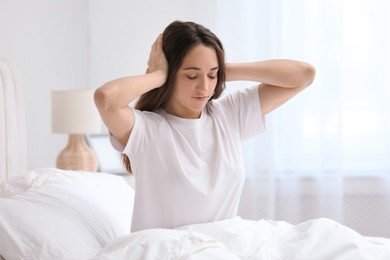 Woman covering ears in bed at home